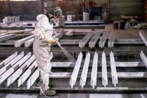mężczyzna maluje metalowe elementy w fabryce