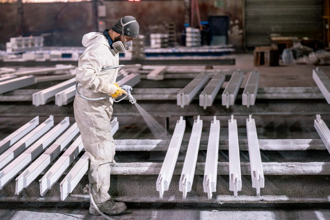 mężczyzna maluje metalowe elementy w fabryce